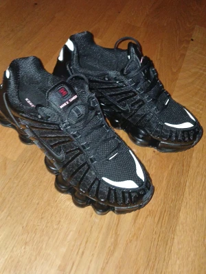 Nike Shox TL svarta sneakers - Nike Shox sneakers i svart med vita och röda detaljer. UTAN BOX Skorna har en unik fjädrande sula, mesh- och syntetmaterial samt snörning. Ikonisk Nike-logga på plösen och hälen. Perfekta för dig som gillar sportig och futuristisk stil.
