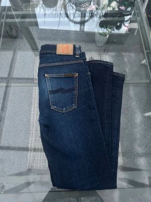 Nudie Grim Tim – Raw Denim Jeans W32 L34 - Säljer Nudie Jeans Grim Tim – Dry True Navy Slim fit jeans i mörkblå raw denim med clean look och snygga detaljer. Riktigt bra fit, funkar perfekt till både streetwear och vardagsfits.  Stretchigt material (99% cotton, 1% elastan) → bekväma men håller formen. Klassisk modell som aldrig går ur stil.  📏 Storlek: W32 L34 👖 Passform: Slim fit 🎨 Färg: Mörkblå / Dry True Navy 📦 Skick: Mycket bra skick  Snabb affär prioriteras ⚡️ Kan skickas direkt. 