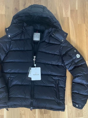 Svart Moncler Maya - Moncler Maya i svart. Riktigt skönt på vintern när det är kallt. Jackan är nyskick. Vid minsta fundering så är det bara att skriva så svarar jag så snabbt jag kan! Storleken är 1, så det är S/M. Pris ej hugget i sten!