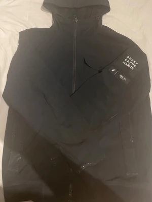 Svart vindjacka från Peak Performance - Snygg svart vindjacka från Peak Performance med  text design på vänstra armen. Fickorna går inte att zipa upp men går att fixa. Små skador på jackan.