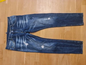 Dsquared2 Slim Jeans Blå, Storlek 52 - Snygga blå slim jeans från Dsquared2 i storlek 52. Jeansen har slitna detaljer, blekta partier och klassisk femficksdesign. Tillverkade i Italien med coolt distressed look och smal passform. Perfekta för dig som gillar streetstyle och exklusiva märken.