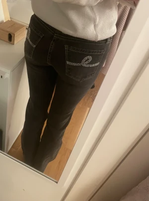 Svarta lowrised vintage jeans - Skigsnygga, lowrised jeans med dekorerade bakfickor från märket Seven7. Några av stenarna saknas på bakfickorna men annars finns det inga problem! Färgen är svart/grå ish med gula sömmar. Storleken på jeansen är 26 