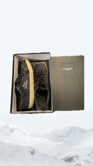 Svarta Saint Laurent sneakers - Svarta sneakers från Saint Laurent med broderad logga på sidan. Skorna har en klassisk låg profil, snörning och beige platt gummisula. Ovandelen är i canvas med detaljer i skinn. Perfekta för dig som gillar en stilren men edgy look.