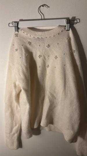 Pärlstickad vit tröja från Stockh LM - Supermysig vit stickad tröja från Stockh LM med pärldetaljer över bröstet och axlarna. Tröjan har rund hals, ribbade muddar och lång ärm. Perfekt för dig som gillar en clean look med lite extra bling. Storleken är ursprungligen M men har krympts i tvätten och passar mer som en XS, kanske även S