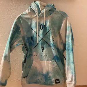 Blå och vit jacka från Dope XXS - Säljer en jacka från Dope i storlek XXS med unikt blått och vitt mönster som påminner om vattenfärg. Jackan har huva med snörning, stor magficka och mjukt fleecefoder på insidan. Perfekt för dig som gillar streetwear och vill sticka ut.