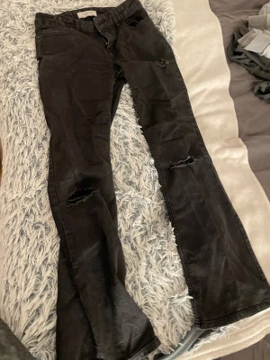 Svarta bootcut jeans från Detroit - Svarta jeans från Detroit (Lindex) med bootcut passform och slitna detaljer på både fram- och baksida. Jeansen har klassisk femficksdesign, bälteshällor och grova hål på benen för en edgy look. Materialet är jeans och färgen är mörk svart. De är i strl 12 år (152), jag är ca 160 och det är därför jag säljer dem. För att de är för korta. Dessa jeans hade kunnat vara fina att göra till shorts eller en jeans kjol med volanger. Pris kan diskuteras och kan skicka fler bilder🥰 De har inga defekter. 