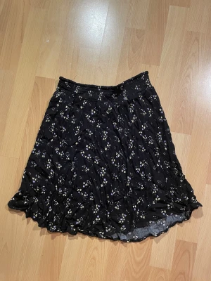 Svart blommig kjol från XOXO Friends - Supersöt svart kjol med små blommor från XOXO Friends. Kjolen är knälånga, har resår i midjan och ett lätt, flowy tyg som ger en avslappnad vibe.