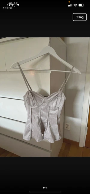  korsett med smala axelband - Säljer en snygg champagnefärgad korsett med smala justerbara axelband. Toppen har markerade sömmar och en lätt glansig finish som ger en lyxig vibe. Passformen är figurnära och toppen har en lätt utsvängd nederkant. Perfekt för att lyfta din outfit.