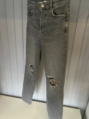 Grå ripped jeans från &Denim - grå jeans från &Denim med slitna detaljer och hål på båda knäna. Modellen har raka ben. Använda fåtal gånger. Kan tyvärr inte visa bild hur dom sitter på då dom är för små för mig. Storlek 34
