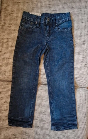 Blå Polo Ralph Lauren 650 jeans - Snygga blå jeans från Polo Ralph Lauren, modell 650. Klassisk femficksdesign med raka ben och normal passform. Jeansen har dragkedja och knapp framtill samt detaljerade bakfickor. Perfekt för dig som gillar tidlös stil och kvalitetsjeans. Den skavank jag har hittat är att är att stygnen som håller fast lappen på baksidan har börjat gå upp. Som storlek står det 4/4T jag skulle nog säga att de motsvarat ca stl 98.