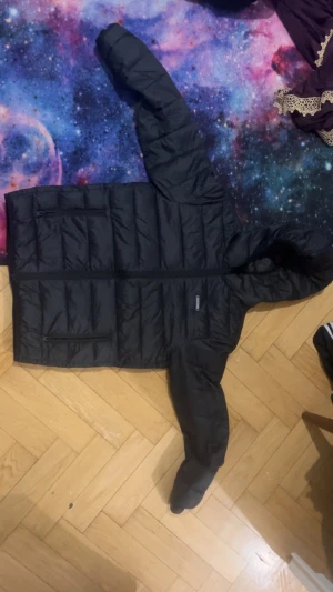 Svart pufferjacka från Jack & Jones - Säljer en svart pufferjacka från Jack & Jones med huva och dragkedja framtill. Jackan har två sidofickor med dragkedja och quiltad design. Perfekt för kyliga dagar och enkel att matcha med olika outfits.