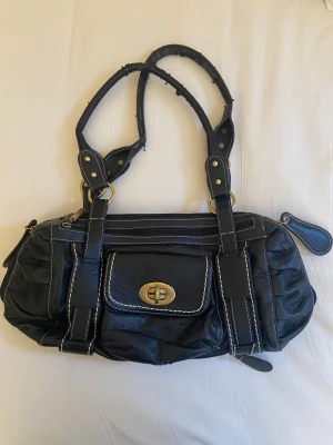 Svart handväska med vita sömmar - Super fin svart handväska. Tyvärr väldigt sliten på handtagen med skinnimitationen som flagnar av. Annars bra skick. Köpt på tradera. 