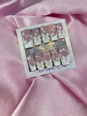 FrenchPearl (M);Medium Square - Säljer ett set med handgjorda press-on naglar i storlek M: 16 mm, 12 mm, 12,5 mm, 11,5 mm, 10 mm. Naglarna har en nude-rosa bas med handmålade vit fransk tippar, dekorerade med 3D-rosetter och pärlformade detaljer. Designen är glansig och söt, perfekt för dig som gillar extra detaljer och en girly vibe.