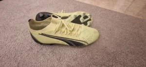 Puma Ultra gula fotbollsskor - Säljer ett par snabba Puma Ultra fotbollsskor i ljusgul och svart färg. Skorna har snörning, platt sula med dobbar och en sportig design med Pumas ikoniska logga på sidan. Ovandelen är tillverkad i syntetmaterial för lätt känsla på planen. Andvända max 3 träningar därav helt i ny skick 