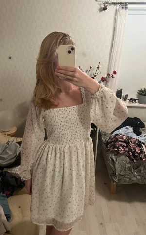 Vit blommig kortklänning Noisy May - Supersöt vit kortklänning från Noisy May med små gula blommor, smockad överdel och långa, transparenta puffärmar. Klänningen har fyrkantig ringning och flowy kjol, perfekt för en somrig look. Materialet känns lätt och luftigt. Endast använd få gånger💞