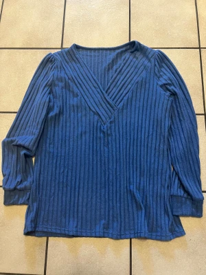 Blå ribbad långärmad tröja - Snygg blå långärmad tröja med ribbat mönster och v-ringad hals. Materialet känns mjukt och stretchigt, perfekt för dig som gillar bekväma och stilrena plagg. Passar dig som vill ha en enkel men ändå cool look med lite struktur i tyget.