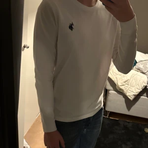 Us polo assn långärmad tröja - Säljer en stilren vit långärmad tröja från Ralph Lauren med den klassiska loggan broderad på bröstet. Tröjan har rund hals och är gjord i mjuk bomull, perfekt för dig som gillar enkel och clean stil. Endast testad