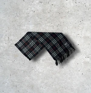 Svart Burberry halsduk - Säljer en tidlös Burberry-halsduk i en djup, mörkgrön färg med det ikoniska rutmönstret. Tillverkad i 100% mjuk och värmande ull som känns lyxig, håller formen väl och ger en exklusiv helhetskänsla. En perfekt accessoar som ger en subtil men sofistikerad färgton till både vardags- och kvällsoutfits.  🧵 Skick: Mycket fint skick, varsamt använd 🌟 Känsla: Mjuk, varm och följsam 📦 Frakt: Skickas tryggt inom 24h 📏 Mått: Längd-150cm, Bredd-30cm Pris kan diskuteras!