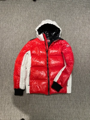 Colmar jacka(ny) - Säljer en fet dunjacka från Colmar i rött och vitt med svart insida på huvan. Jackan har en schysst puffer-look, dragkedja framtill och ribbade muddar vid ärmslut. Perfekt för dig som vill sticka ut i vinterkylan. Logga på ärmen och huva för extra stilpoäng.