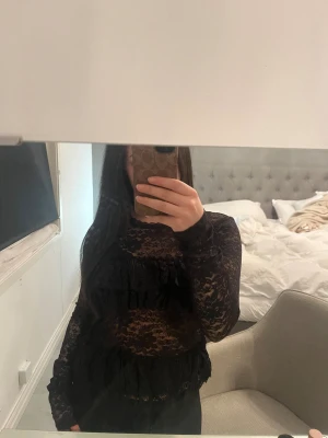 Svart spetsblus med volanger - Säljer en svart långärmad blus i spets från nelly med volangdetaljer över bröstet och midjan. Blusen är genomskinlig och har ett blommigt spetsmönster. Använd fåtal gånger och inga synliga defekter!