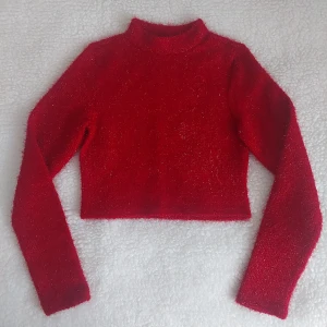 Röd glittrig stickad tröja - Snygg julröd tröja från H&M Divided i croppad modell med lång ärm. Tröjan har glittriga detaljer och är tillverkad i mjuk polyester som ger en fluffig känsla. Perfekt för dig som vill sticka ut med lite extra glitter och färg till jul och nyår. I nyskick då den bara är anvönd en jul. Från rök och djurfritt hem