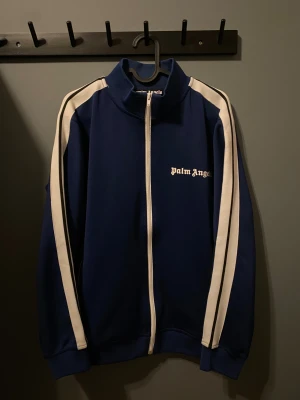 Marinblå Palm Angels  - Säljer en snygg marinblå tröja Palm Angels med vita ränder längs ärmarna och vit dragkedja. Den är bara använd ett fåtal gånger så är väldigt bra skick. Jag säljer den för 699 vilket är ett bra pris eftersom dessa brukar kosta kring 3000-: på andrahandsmarknaden. Om du vill göra dig en bra affär så är det bara att höra av sig!