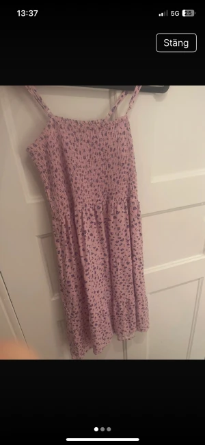 Ljusrosa blommig sommarklänning  - Supersöt ljusrosa kort klänning köpt på New yorker med lila blommigt mönster. Smockad upptill och med smala, justerbara axelband. Perfekt för varma dagar och ger en riktigt fräsch vibe. Tunn och luftig, passar dig som gillar en feminin och avslappnad stil.