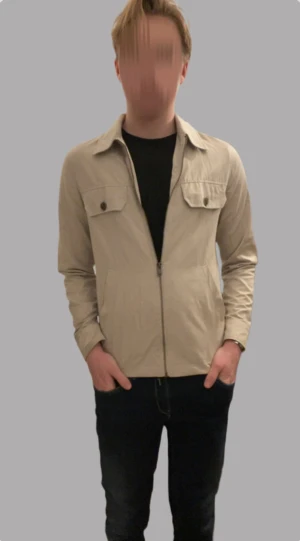 Beige overshirt från River Island XS - Stilren beige overshirt från River Island i storlek XS. Jackan har klassisk krage, två bröstfickor med knappar och dragkedja framtill. Perfekt för lager-på-lager och enkel att matcha med olika outfits.