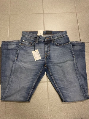 Blå tiger of Sweden jeans W28 L32 - Snygga blå jeans med klassisk femficksdesign och raka ben. Jeansen har en brun patch bak i midjan och detaljerade sömmar på bakfickorna. Tillverkade i slitstarkt denim med en något smalare fot. Perfekta för dig som gillar en clean och tidlös look.