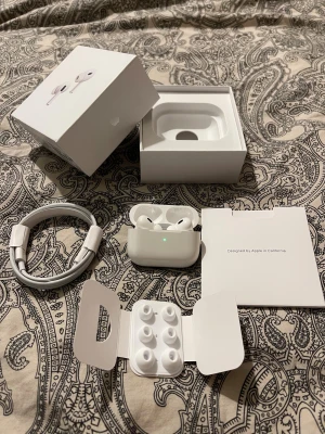 AirPods Pro 2- giltig AppleCare, komplett  - Absolut, här är en uppdaterad version:  Säljer ett par original AirPods Pro (2:a generation) i fungerande skick.  AppleCare till 17 maj 2026 - överförs automatiskt till dig vid köp.  Komplett förpackning, kartong, USB-C kabel och extra öronpluggar.  Serienummer stämmer överens med boxen och fodralets insida, på AirPodsen och iPhone inställningar. Batteriets hälsa är som ny. Kommer från rök- och djurfritt hem. Perfekt julklapp! Vid frågor är det bara att fråga.