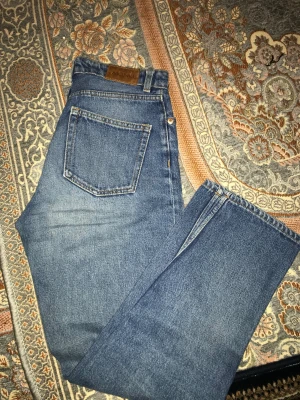 Blå raka jeans från Monki, storlek 25 - Säljer ett par klassiska blå jeans från Monki i storlek 25. Jeansen har hög midja, raka ben och femficksmodell. Tillverkade i 100% bomull för en äkta denimkänsla. Perfekta för dig som gillar en tidlös och clean look.
