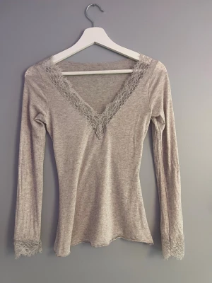 Beige intimissimi topp med spets - Säljer en beige långärmad topp från intimissimi  med v-ringning och fina spetsdetaljer vid halsringningen och ärmsluten. Inga defekter.