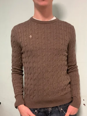 Morris kabelstickad merinoull tröja brun/grå  - Snygg grå/brun kabelstickad tröja från Morris i 100% merinoull. Klassisk rund halsringning och diskret vit logga broderad på bröstet.  Mycket bra skick, förutom 2 små hål.  Storlek m men sitter som en s. Bara att höra av dig om du har några frågor. Allt gott deluxe garderoben🤩 
