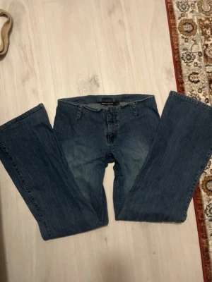 Blå bootcut jeans från DKNY - Snygga blå jeans från DKNY med klassisk bootcut-passform och normal midja. Jeansen har dragkedja och knapp framtill samt bälteshällor. Materialet är jeans med lätt tvättad look och raka ben som blir bredare nedtill. Perfekt för dig som gillar retrovibbar.