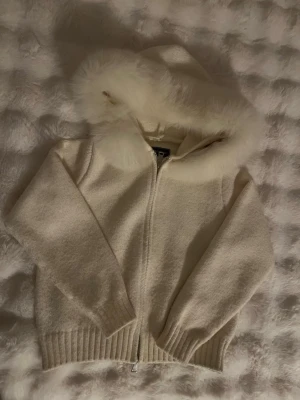 Vit cardigan med äkta rävpäls från Alessa - Säljer en vit cardigan från Alessa med huva och avtagbar äkta rävpäls. Jackan har dragkedja framtill och ribbade muddar vid ärmslut och nederkant. Perfekt för dig som vill ha en mysig och stylish look under kyliga dagar. Jag har använt den max 5 gånger så jackan är inprincip ny, den är i väldigt bra skick!! Pris kan diskuteras! 