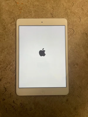 iPad Mini - Apple iPad Mini i silver med vit front. Skärmen startar och visar Apple-loggan. Baksidan har mindre repor och märken, men överlag gott skick. Perfekt för surf, appar och underhållning. Säljs utan tillbehör.