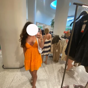 Kort orange klänning med volang - Superfin kort klänning i starkt orange med volangkant och v-ringning. Ärmlös modell med luftig passform, perfekt för varma dagar. Snygg och enkel att styla med sandaler eller sneakers.