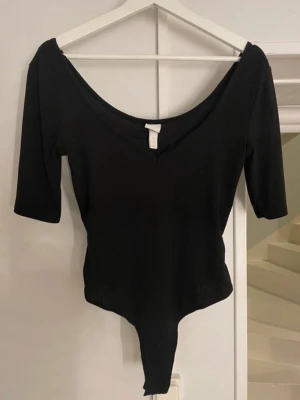 Svart ribbad body från H&M - Svart body med ribbad struktur från H&M, har en djup v-ringad hals och halvlånga ärmar. Helt oanvänd!!!