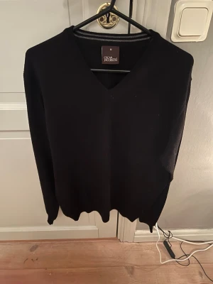 Svart v-ringad tröja Oscar Jacobson - Svart v-ringad tröja från Oscar Jacobson i storlek M. Klassisk och stilren design med långärmade ärmar och ribbade muddar. Perfekt för dig som gillar en enkel look med lite edge. Materialet känns mjukt och är troligtvis bomull eller ull. Kan sänka pris vid snabb affär.
