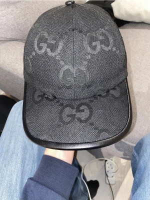 Svart Jumbo Keps - Kepsen har en böjd skärm med läderkant och justerbart spänne i läder baktill. Materialet är robust och har en exklusiv känsla, perfekt för dig som gillar designeraccessoarer.