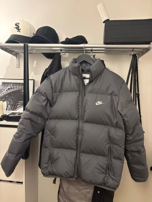 Grå Nike Therma-Fit pufferjacka XS - Säljer en grå pufferjacka från Nike i modellen Therma-Fit. Jackan har hög krage, två dragkedjeförsedda fickor och broderad Nike-logga på bröstet. Inköpt för två månader sen kvitto finns. Säljer då jag ej använder. 