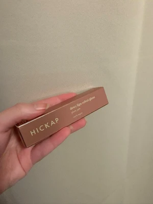 Dewy Lips Velvet Gloss Plum Jam - Läppglans från Hickap i nyansen Plum Jam, en djup plommonlila färg med sammetslen finish. Kommer i en stilren tub med beige lock och applikator för enkel applicering. Perfekt för dig som vill ha glossiga och fylliga läppar med en trendig färg.