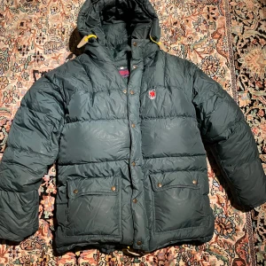 Mörkgrön expedition dunjacka från Fjällräven M - Säljer en mörkgrön expedition dunjacka från Fjällräven i storlek M. Jackan har huva, stora fickor med knappar och dragkedja framtill. Perfekt för kalla dagar. Några få skavanker  men därav det billiga priset. :)