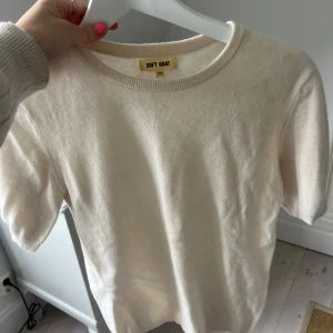 Beige kashmirtröja från Soft Goat - Supermjuk och lyxig beige kashmirtröja från Soft Goat i storlek XS. Tröjan har rund hals, korta ärmar och ribbade kanter vid hals och nederkant. Perfekt för dig som gillar stilrena och sköna plagg med premiumkänsla.