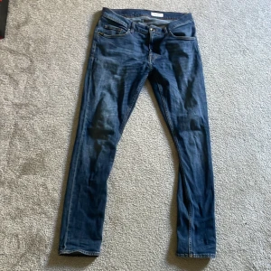 Blå jeans från Tiger of Sweden - Snygga blå jeans från Tiger of Sweden med klassisk femficksdesign och läderpatch bak i midjan. Jeansen har smal passform, raka ben och är tillverkade i mjukt denimtyg med lätt tvättad look. Perfekta för dig som gillar stilrena och tidlösa jeans.