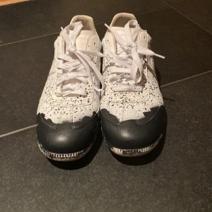 Maison Margiela gats - Maison Margiela sneakers i vitt skinn med svart färgdetalj på tån och coolt stänkmönster över hela skon. Storlek 44 och använda ca 10 gånger. Säljer pga att dom var för små och gillar inte färg stänket 