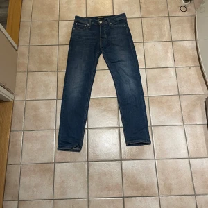Jack & Jones Slim Glenn jeans blå 29/30 - Mörkblå jeans från Jack & Jones, modell Slim Glenn. Snygg slim fit med klassisk femficksdesign och gul kontrastsöm. Jeansen är tillverkade i stretchig denim för en bekväm passform och har en modern, smal siluett. Aldrigt använt 