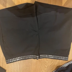 Svarta shorts med nitar från Zara Basic - Snygga svarta shorts från Zara Basic med raka ben och coola silvriga nitar längs bensluten. Perfekta för dig som vill ha en stilren men edgy look. Materialet känns mjukt och bekvämt, och shortsen har en klassisk passform.