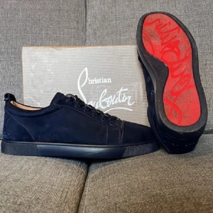 Svarta sneakers från Christian Louboutin - Snygga svarta sneakers från Christian Louboutin i mocka med klassisk röd sula och diskret logga på sidan. Skorna har rund tå, snörning och en stilren design som passar perfekt till streetwear eller en mer dressad look. Kvitto ingår självklart! Snabb affär prioriteras! 