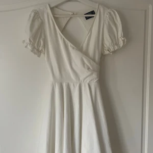 Vit klänning med puffärm - Supersöt vit kortklänning från NA-KD med omlottliv, puffiga kortärmar och öppen rygg. Perfekt för student och liknande.